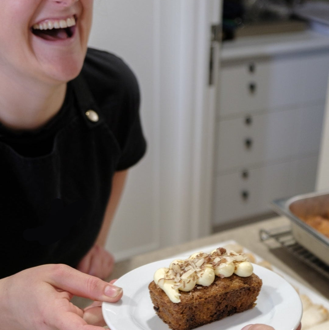 A person is served a plate with a sandwich and a side of a sweet treat, possibly a scone or a brownie, in a kitchen or dining setting.