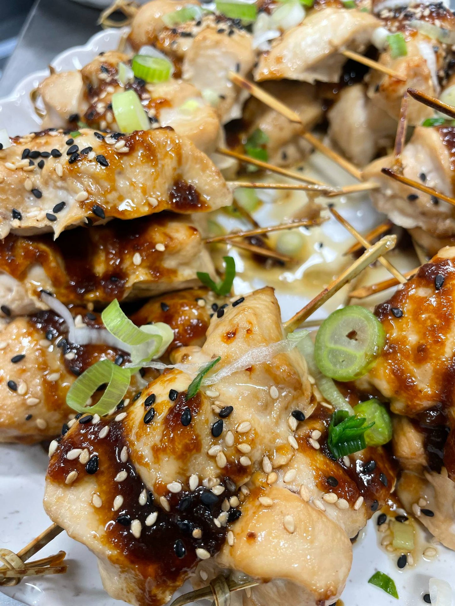 Chicken skewers with sesame seeds and green onions on a white plate