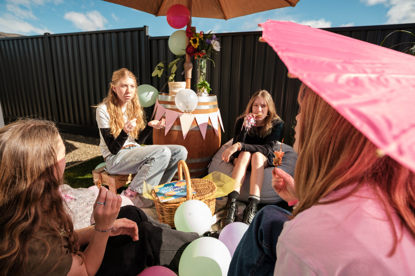 Group of people sitting outdoors with balloons and a pink umbrella