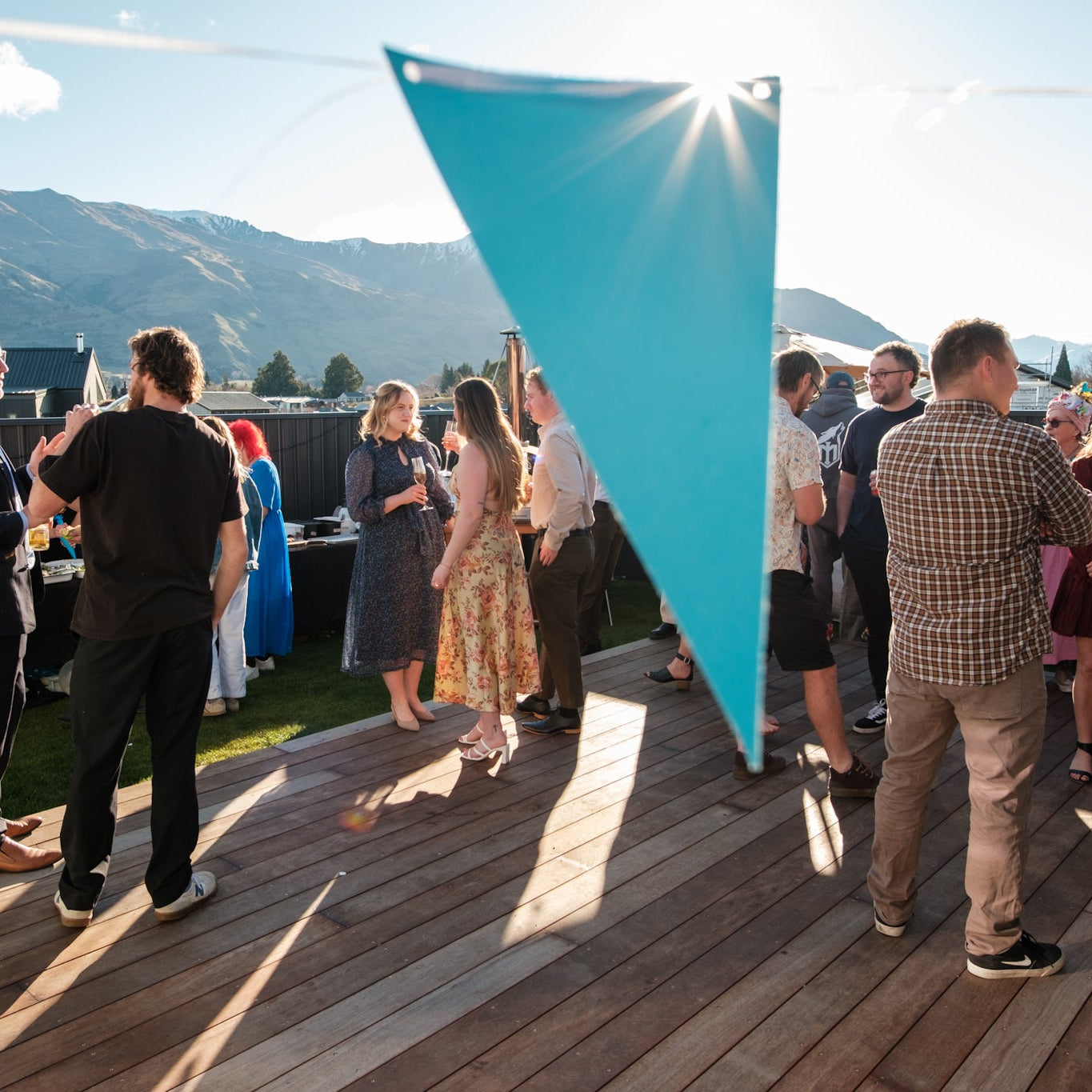 Group of people socializing on a wooden deck with mountains in the background