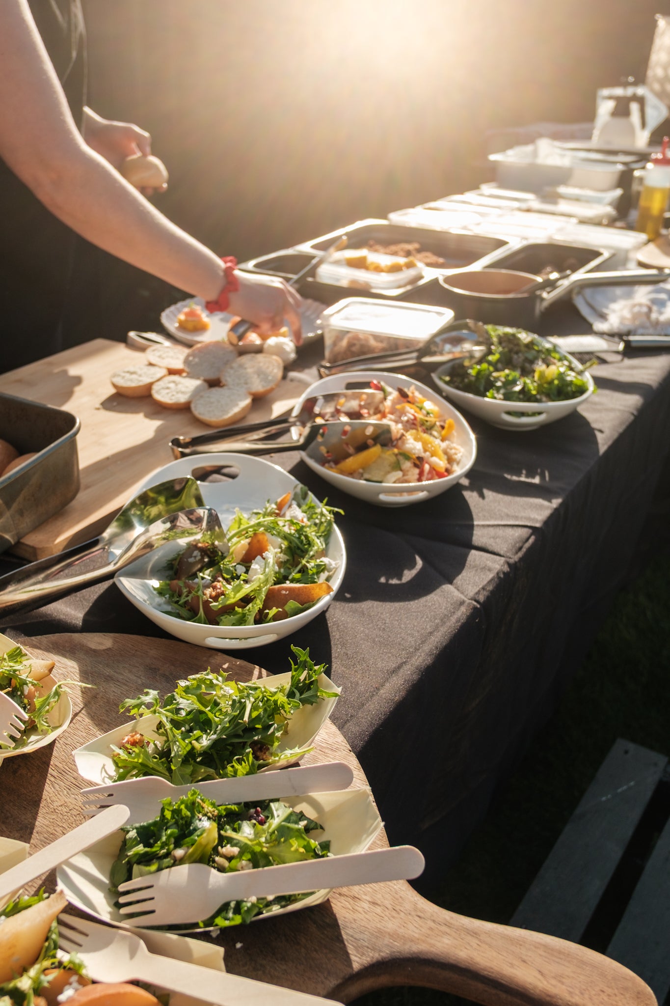 Outdoor setting with a table full of salads and utensils, sunlit.