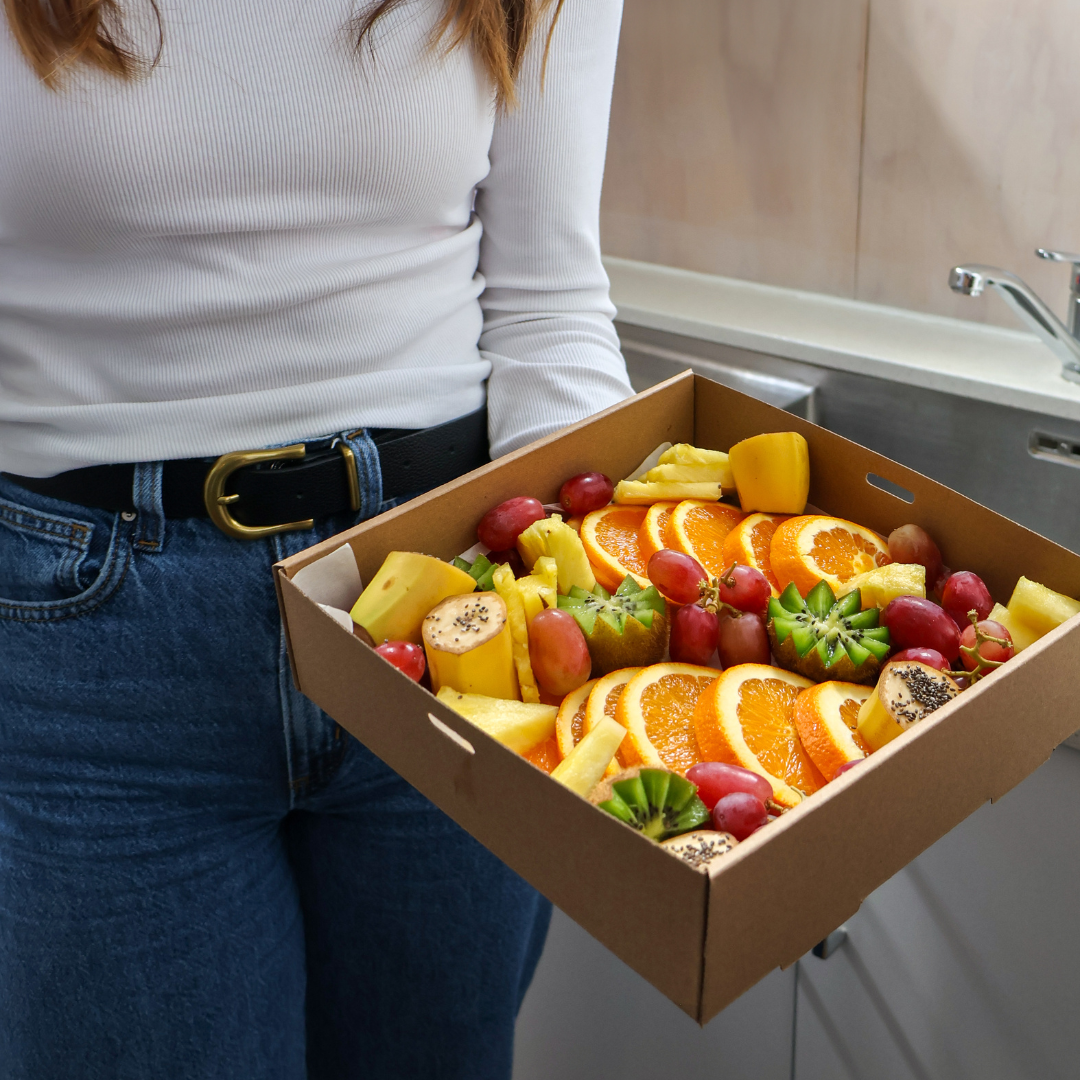 Person holding a box of assorted fruits in a kitchen setting