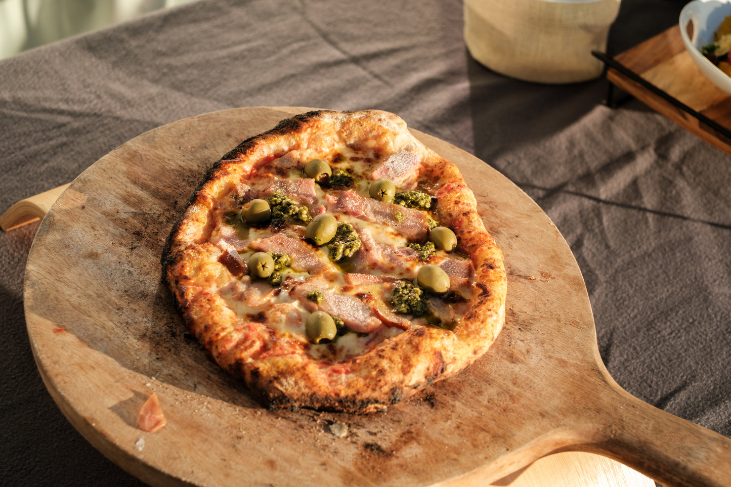 Pizza with olives, ham and pesto on a wooden board