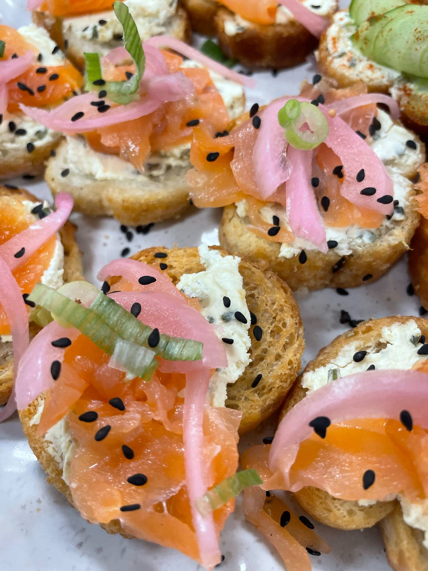 Smoked salmon canapés with cream cheese, pink onions, and wasabi on a white plate.