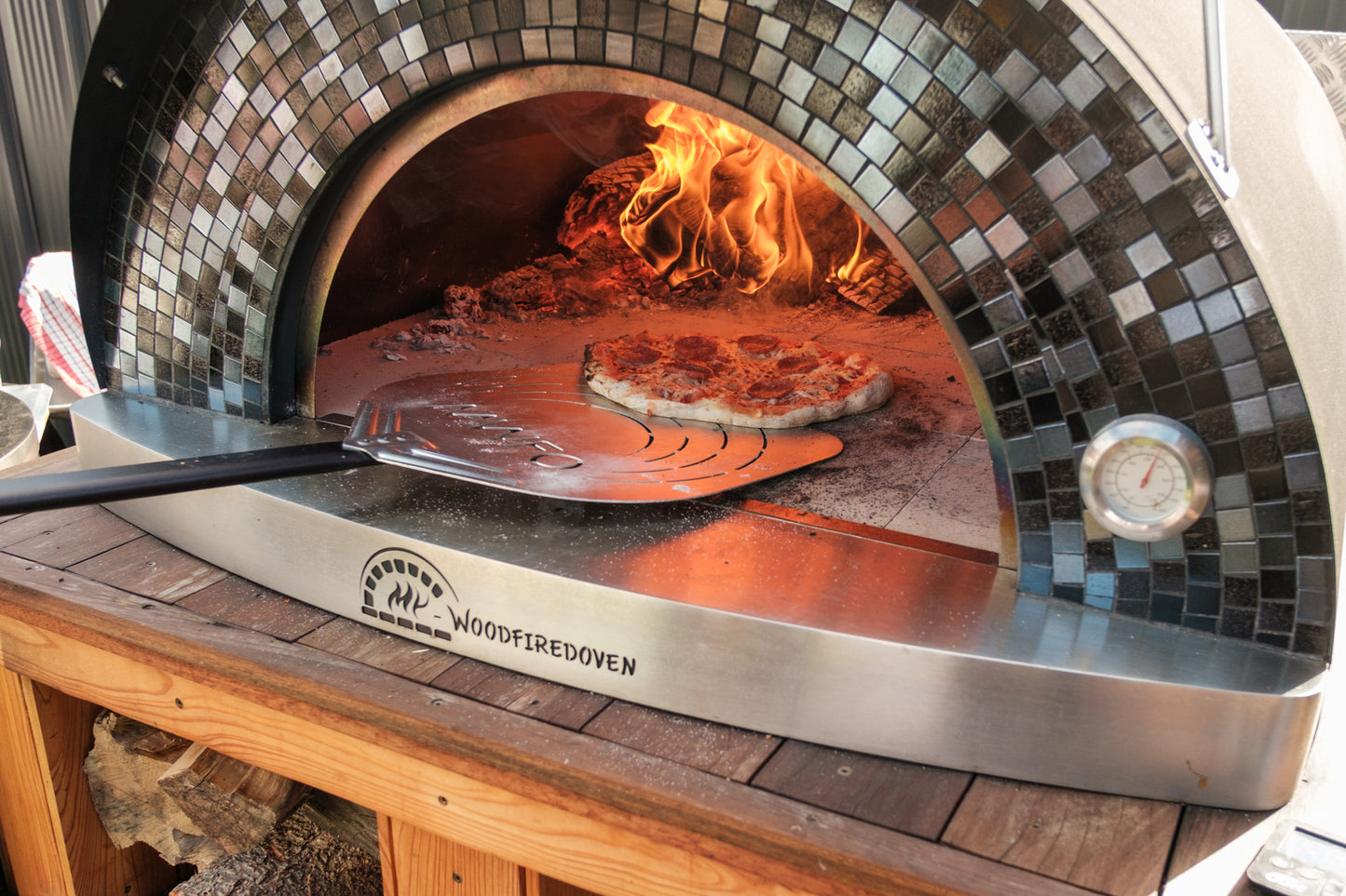 Wood-fired oven with pizza being cooked inside, on a wooden table.