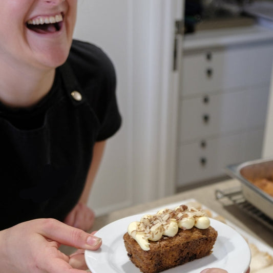 A person is served a plate with a sandwich and a side of a sweet treat, possibly a scone or a brownie, in a kitchen or dining setting.