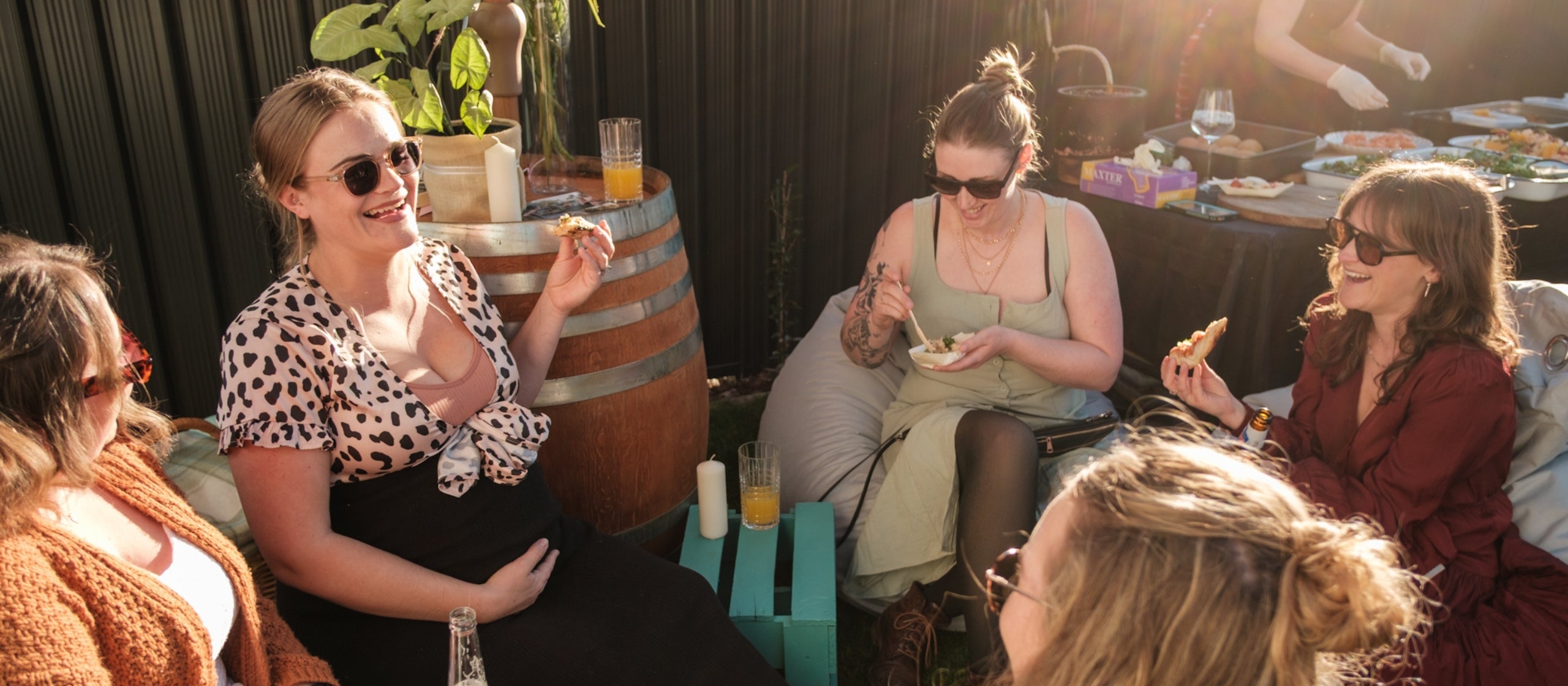 Group of women sitting outdoors, enjoying drinks and food, with a casual and relaxed atmosphere.