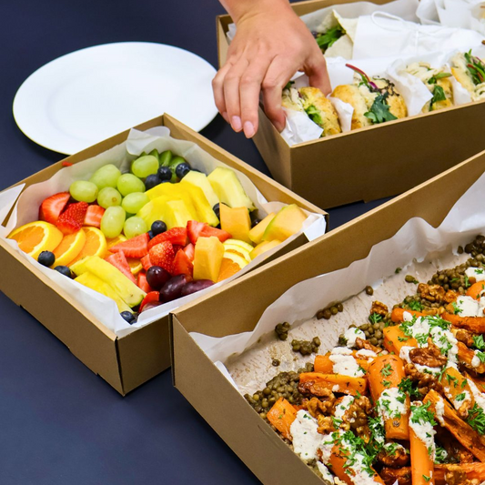 Three cardboard boxes containing different types of food on a dark surface.